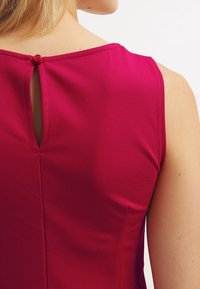 Magenta ärmelloses Kleid mit einem dezenten Rückenausschnitt und einem dekorativen Knopf am Hals. Glatte Stoff mit leichtem Glanz.