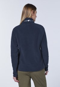 Navy blue fleece pullover with a high collar and embroidered logo on the neck. Features a soft texture and fitted sleeves.