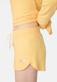 Pantaloni corti gialli in cotone con orlo a scalloped, caratterizzati da un motivo floreale ricamato e una vita con cordoncino regolabile.