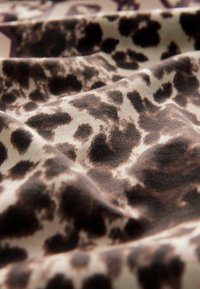 Leopardmønstret stof med en blød tekstur; har mørkebrune pletter på en lys beige baggrund, der afslører folder og dybde.