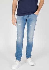 Jeans de denim azul claro con un corte ajustado, que presentan detalles desgastados y un efecto de desvanecimiento. Combinados con zapatillas blancas y una camiseta azul marino.