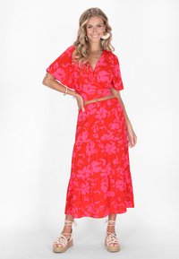 Set a due pezzi floreale rosso con maniche corte e gonna a più strati. Il motivo presenta grandi fiori rosa su uno sfondo rosso vivace.