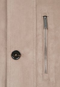 Beige faux suede jacket featuring a black button closure and a silver zipper pocket, with visible stitching details.