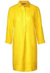 Vestido de lino amarillo con cuello, tapeta de botones y mangas tres cuartos. Presenta un corte relajado y aberturas laterales en el dobladillo.