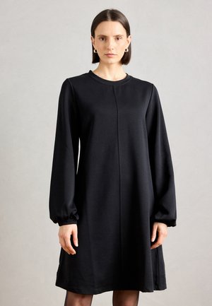 Abito nero a maniche lunghe con vestibilità morbida, scollo rotondo e polsini arricciati. Texture liscia con un dettaglio di cucitura centrale.