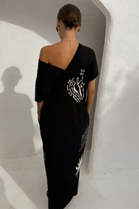 Czarna długa sukienka z odkrytymi ramionami, ozdobiona białymi motywami graficznymi i wycięciem na plecach. Miękki materiał o luźnym kroju.