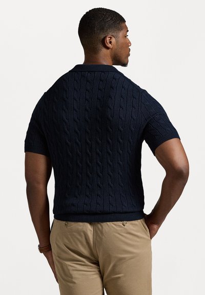 Μπλέ πλέκτο πόλο κοντομάνικο με σχέδιο καλωδίων, διαθέτοντας σταθερό ριχτό γιακά και στρίφωμα. Ο σχεδιασμός είναι εφαρμοστός με λεία υφή.
