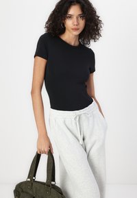 Sort, tætsiddende top med korte ærmer parret med lysegrå sweatpants, der fremviser en afslappet silhuet. Modellen holder en struktureret olivengrøn taske.