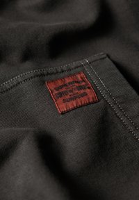 Black fabric with a textured finish features a stitched red label displaying the brand name "Superdry" and care instructions.