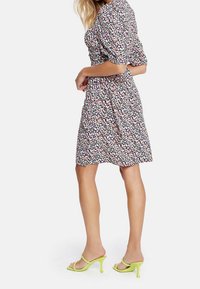 Kleid mit floralem Muster, kurzen Puffärmel, tailliertem Schnitt und knielanger Rocklänge. Ergänzt durch grüne offene High Heels.