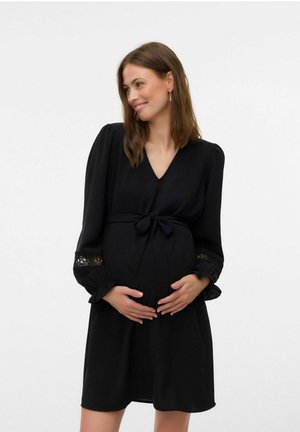 Robe de maternité noire avec un col en V, des manches bouffantes, des accents en dentelle aux poignets et une taille nouée pour mettre en valeur une silhouette fluide.