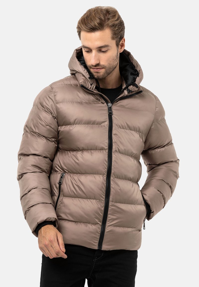Puffjacke in Hellbraun, aus glänzendem Material, mit Kapuze, Zickzacknähten, Frontreißverschluss und seitlichen Taschen mit schwarzen Akzenten.