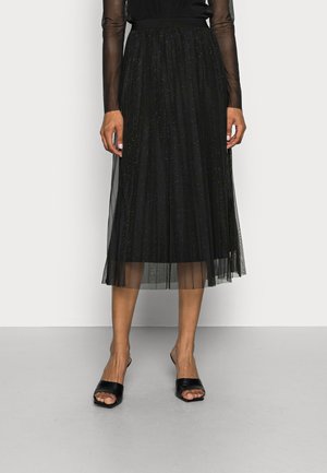 Black tulle skirt with a pleated design, featuring subtle metallic speckles. Paired with black open-toe heeled sandals.