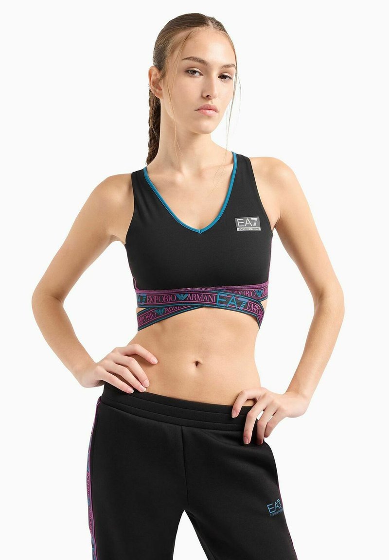 Reggiseno sportivo nero con scollatura a V, bordatura blu e fascia elastica con logo. Abbinato a pantaloni della tuta neri con strisce laterali e dettagli.