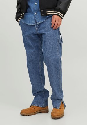 Blaue Denim-Cargohosen mit Seitentaschen, lässiger Passform, fransigem Saum und markanter Naht, kombiniert mit braunen Schnürboots.