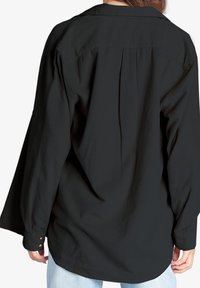 Felpa nera a maniche lunghe con texture a costine, polsini con bottone e vestibilità morbida. Pieghe posteriori per ulteriore libertà di movimento e comfort.