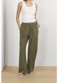 Pantalons larges légers couleur vert olive avec une taille élastique et des poches latérales, associés à un débardeur blanc et des tongs beiges.