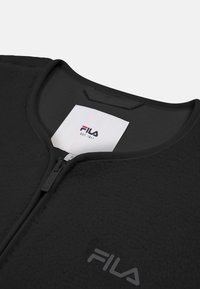 Chaqueta negra de Fila con tejido texturizado, cierre de media cremallera en la parte delantera y pequeño logotipo de la marca en la parte inferior izquierda. Etiqueta visible dentro del collar.