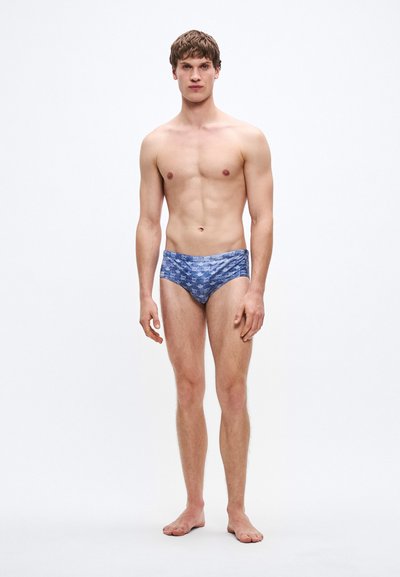 Bañador tipo slip en tela azul con un patrón de pequeñas formas geométricas. Cintura elástica, diseño ajustado y textura suave.