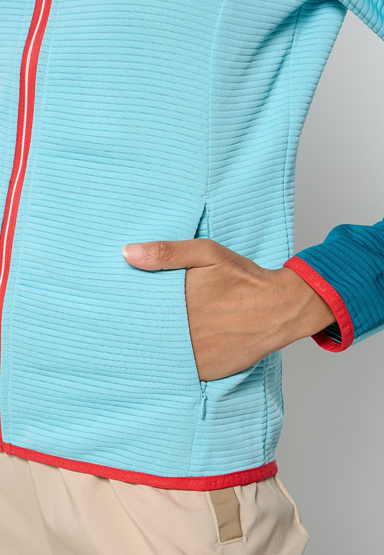 Veste texturée bleu clair avec fermeture éclair rouge à l'avant, accents rouges sur le col et l'ourlet, et une manche bleue. Elle dispose d'une poche latérale.