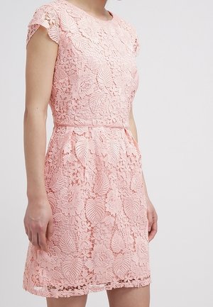 Roze jurk tot op de knie met bloemig kantpatroon, korte mouwen en een getailleerde taille, gedragen door een persoon tegen een effen achtergrond.