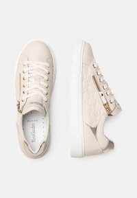 Beżowe sneakersy wykonane z gładkiej skóry z teksturowanym panelem, z elementami w kolorze złotym, sznurowadłami i bocznym zamkiem błyskawicznym. Biała gumowa podeszwa.