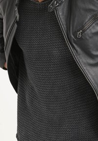 Svart läderjacka med silverdetaljer över en strukturerad mörk stickad tröja. Tröjan har ett ribbat mönster och en lös passform.