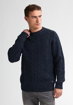 Suéter de punto azul marino con un patrón de trenzas, cuello redondo y puños y dobladillo acanalados. Confeccionado en una tela gruesa y texturizada.