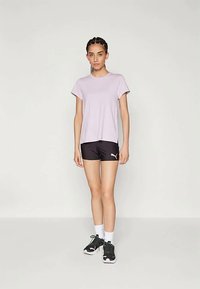 Lyselilla crew-neck t-skjorte kombinert med svarte tettsittende shorts med en rosa logo. Modellen har på seg svarte joggesko og hvite sokker.