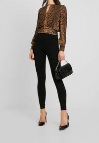 Brun leopardmönstrad blus med nyckelhålsringning, i kombination med svarta leggings. Svart texturerad handväska med kedjestöv och svarta högklackade skor.