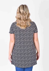 Black tunic with white floral print, short sleeves, and a rounded hem. Smooth fabric, worn over blue jeans. Back view shown.