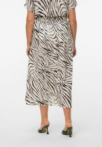Zebramuster Midi-Kleid mit Taillierung; aus leichtem Stoff. Hat einen neutralen Hintergrund mit schwarzen Streifen. Grüne Absatzsandalen.