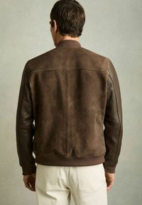 Jachetă din piele maro cu panouri din suede și piele texturată. Mansete și tiv cu model ondulat. Prezintă un design simplu, elegant.
