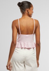 Rosa peplum-top med tynne stropper og teksturert stoff, med en bred bunnkant. Bært med kremfargede cargo-bukser.