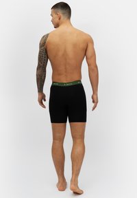 Schwarze Boxershorts mit einem grünen elastischen Bund, aus einem glatten Stoff gefertigt, für eine enge Passform, von hinten gesehen.