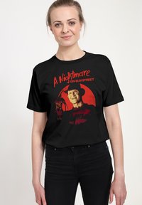 Černé bavlněné tričko s grafickým designem a červeným a oranžovým nápisem "Noční můra v Elm Street" a ilustrací postavy.