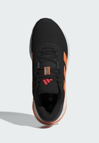 Zwarte sportschoen met oranje accenten, gestructureerde bovenkant, veters en drie-strepenlogo. Witte zool met een subtiele gradient. Lichtgewicht ontwerp.