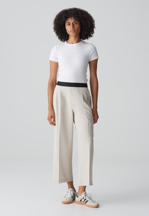 White ribbed short-sleeve top, beige wide-leg trousers with a black elastic waistband, paired with gray and black sneakers. Smooth texture.