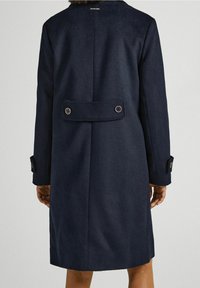 Cappotto di lana blu navy visto da dietro, con dettaglio a doppio bottone e una silhouette pulita e sartoriale.