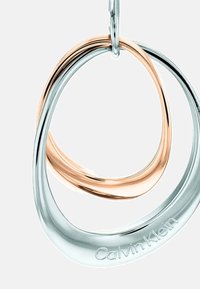 Pendientes aros entrelazados en plata y oro rosa con un acabado suave y pulido, que cuentan con un grabado de la marca en la pieza de plata.