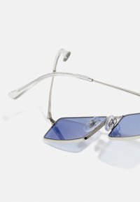 Silverfärgade metallsunglasses med blåtonade linser, geometriskt formade bågar och genomskinliga nässkydd, med eleganta, tunna skalmar.