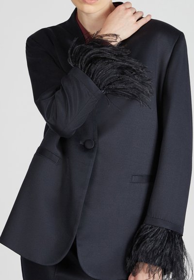 Czarna marynarka z jednym guzikiem, z fakturowanym czarnym frędzlem przy mankietach i gładkim materiałem, dopasowanej konstrukcji oraz klasycznymi klapami.