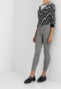 Black and white zigzag-patterned sweater with long sleeves paired with gray plaid leggings and shiny black lace-up shoes.