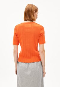 Pull court à manches courtes en rib à col rond de couleur orange, avec une silhouette ajustée et un motif texturé subtil.