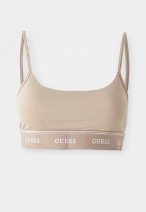 Beige croptop bralette gjort av slätt tyg, med tunna band och en midjeband med vit "GUESS" logotyp. Enkel, sömlös design.