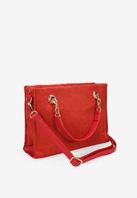 Bolsa de tela roja con forma estructurada, que presenta herrajes dorados y dobles asas. Strap de hombro ajustable adjunto. Textura suave.