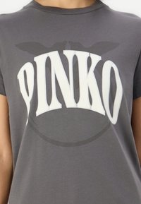 Camiseta de algodón gris con cuello redondo y mangas cortas, que presenta un gran logo blanco de "PINKO" exhibido de manera prominente en el centro.