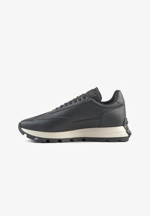 Crna niska tenisica s crnim vezicama, bijelim srednjim tabanom i grubim crnim potplatom prikazana iz bočnog profila na bijeloj pozadini.