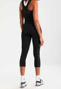 Top sportivo nero senza maniche e leggings capri con motivo testurizzato e dettagli riflettenti. Il modello indossa scarpe sportive e calze.