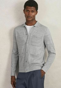 Hellgraue Strickjacke aus weichem Material, mit Kragen, Knopfverschluss, einer Vordertasche und zwei Seitentaschen. Lange Ärmel.